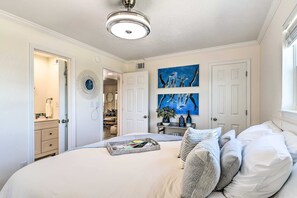 Un dormitorio con cama, mesitas de noche, ventilador de techo y obras de arte en la pared.