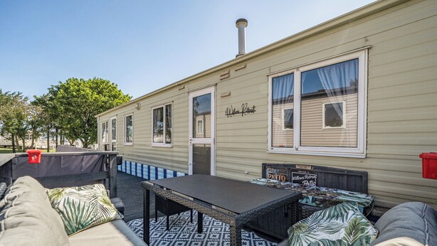 Una casa móvil con un patio que incluye una mesa, sillas, un sofá y un tapete estampado.