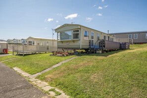 A mobile home with a large window, a porch, and a small garden area. - 3 Bed - Sleeps 8 - Sea View - Pets - Parking (Reighton Gap)
