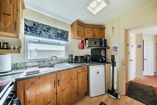 A compact kitchen with wooden cabinets, a built-in microwave, a coffee maker, and a refrigerator.
