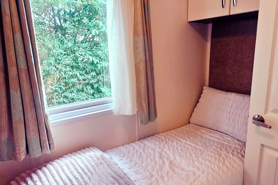 Een slaapkamer met een enkel bed, een raam met gordijnen en een deur.