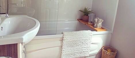 A bathroom with a white bathtub, a sink, and a shower. There is a wicker basket and a small plant on the shelf.