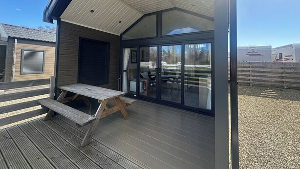 A covered outdoor area with a wooden bench, a sliding glass door, and a view of a fenced area with RVs.