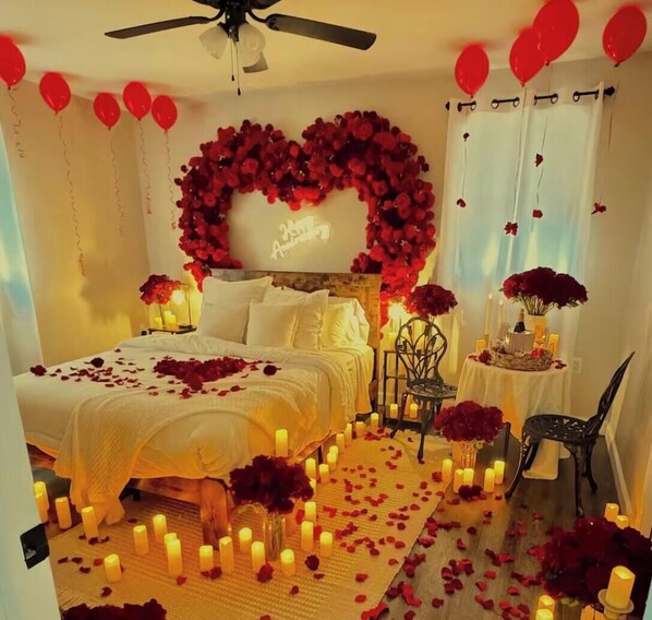 A room with a bed, a heart-shaped floral arrangement, candles, and red balloons.