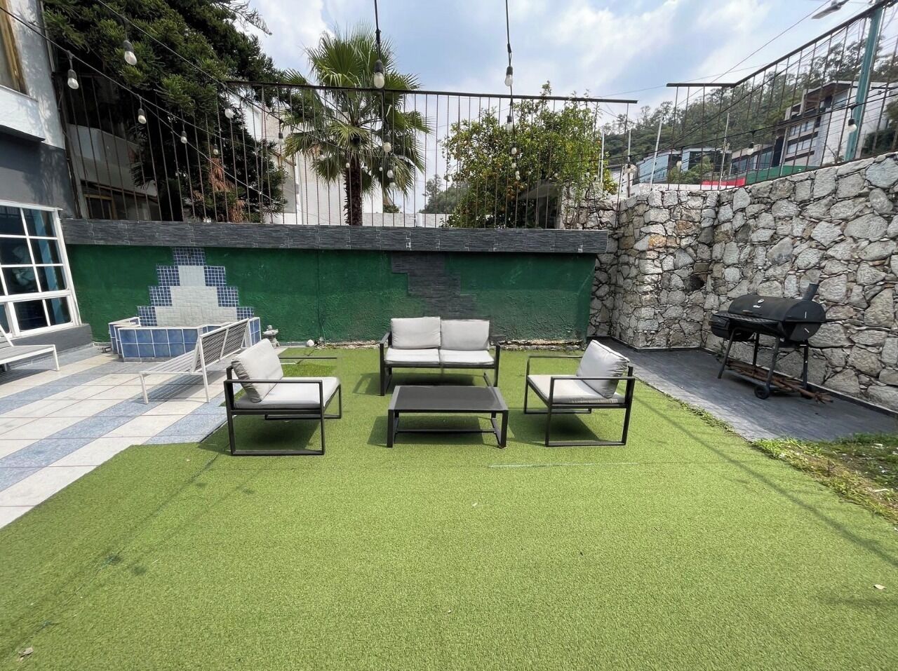 Zona d'estar a l'aire lliure amb gespa artificial, una paret de pedra i una barbacoa.
