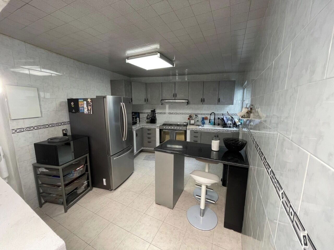 A modern kitchen with stainless steel appliances, a central island with bar stools, and a tiled backsplash.