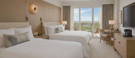 A hotel room with two beds, a ceiling fan, a TV, a desk with a chair, and a balcony with a view.