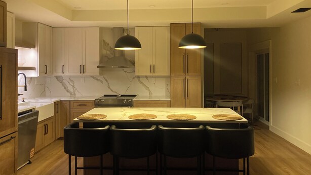 Una cucina moderna con isola centrale, sgabelli da bar, illuminazione a sospensione e zoccolo in marmo.