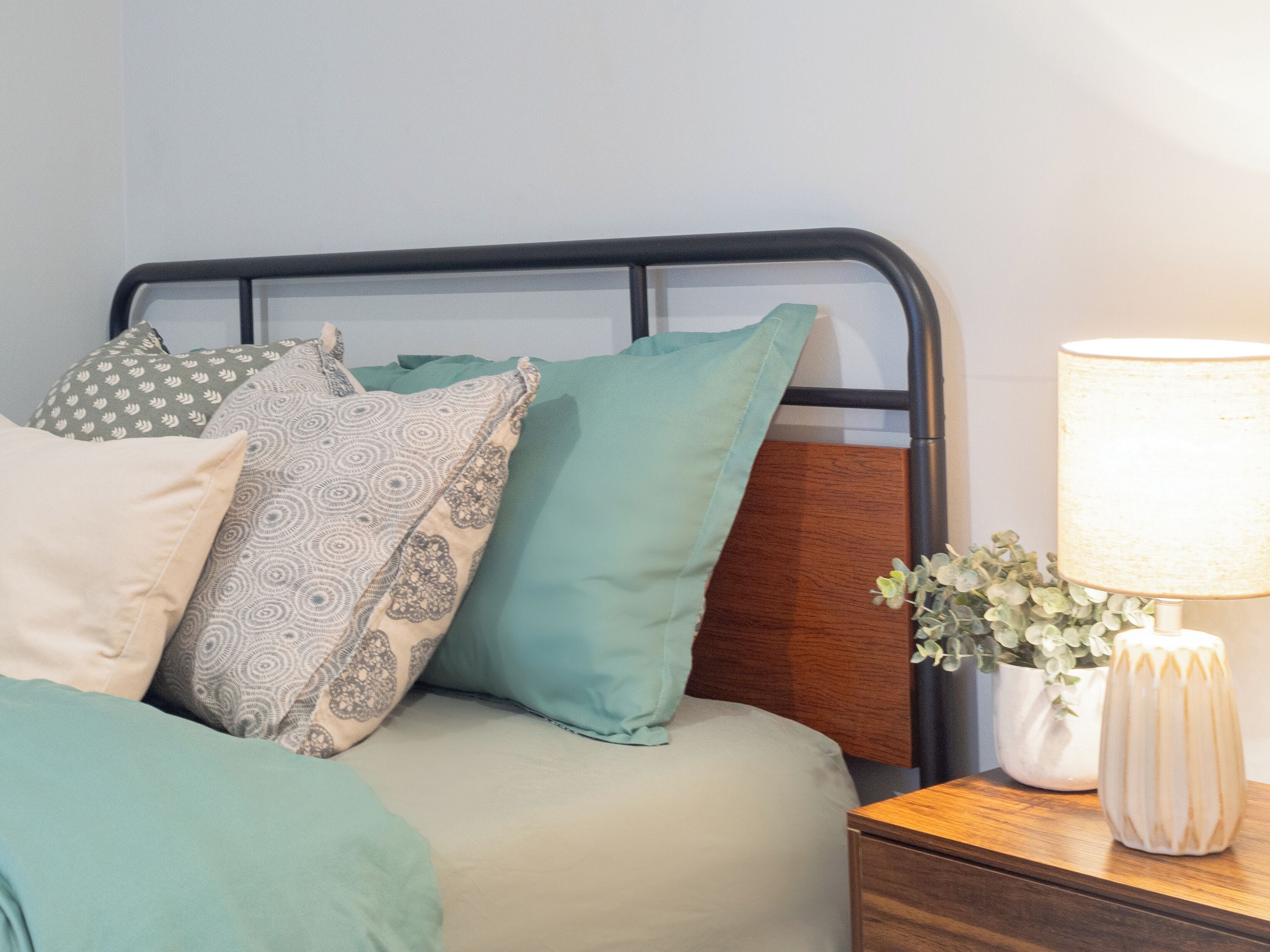 Un lit avec une tête de lit, plusieurs oreillers, une table de chevet avec une lampe et une plante en pot.
