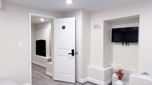 Una habitación moderna con una puerta blanca, una chimenea, un televisor montado y un pequeño jarrón blanco con plantas secas.