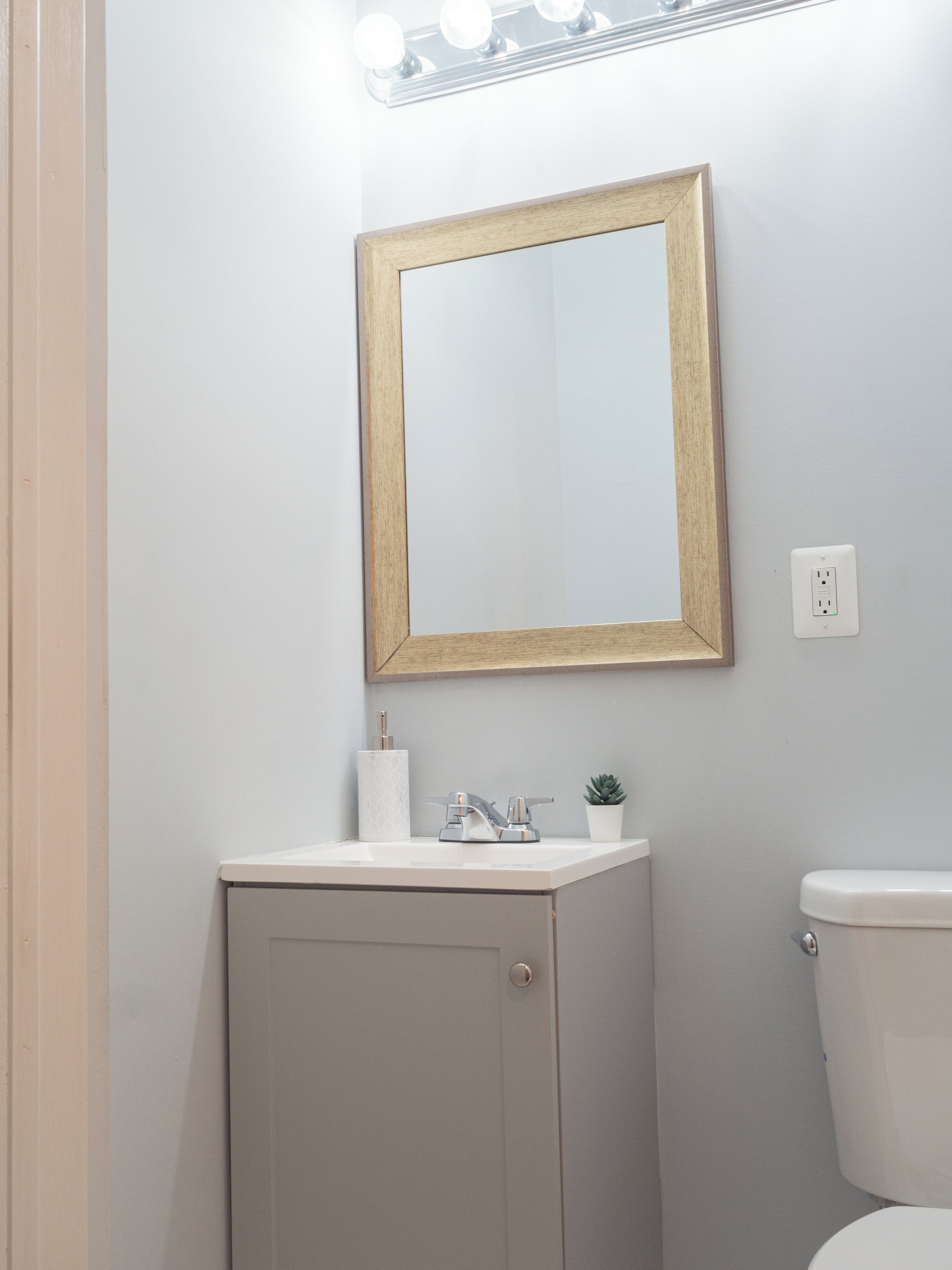 A bathroom with a white sink, a mirror with a wooden frame, a toilet, and a small potted plant on the sink.