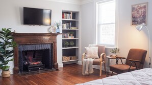 Una habitación acogedora con chimenea, una estantería, un sillón cómodo y una cama.