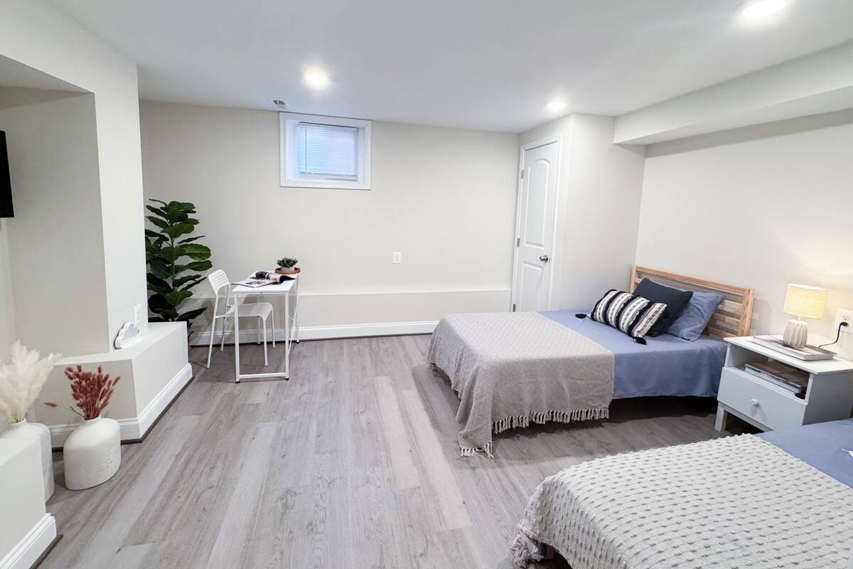 A bedroom with two beds, a desk, a chair, a window, and a plant.