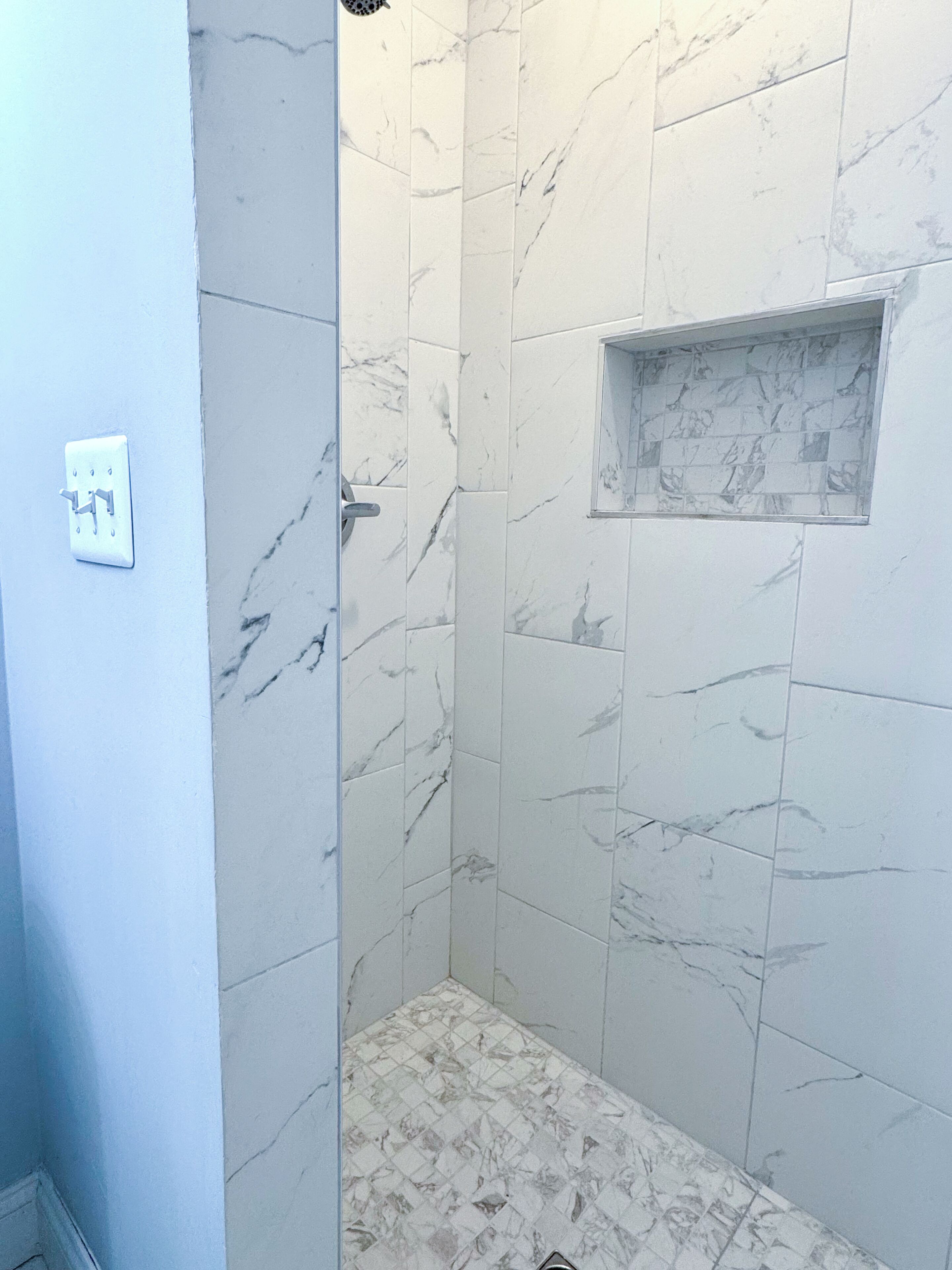 Une salle de bain avec des carreaux de marbre blanc et une petite fenêtre.