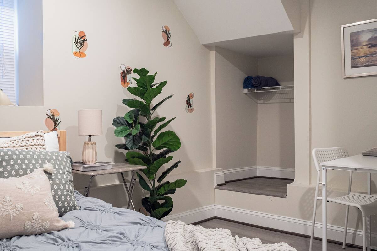 A bedroom with a bed, bedside table, lamp, potted plant, and a view of a balcony.