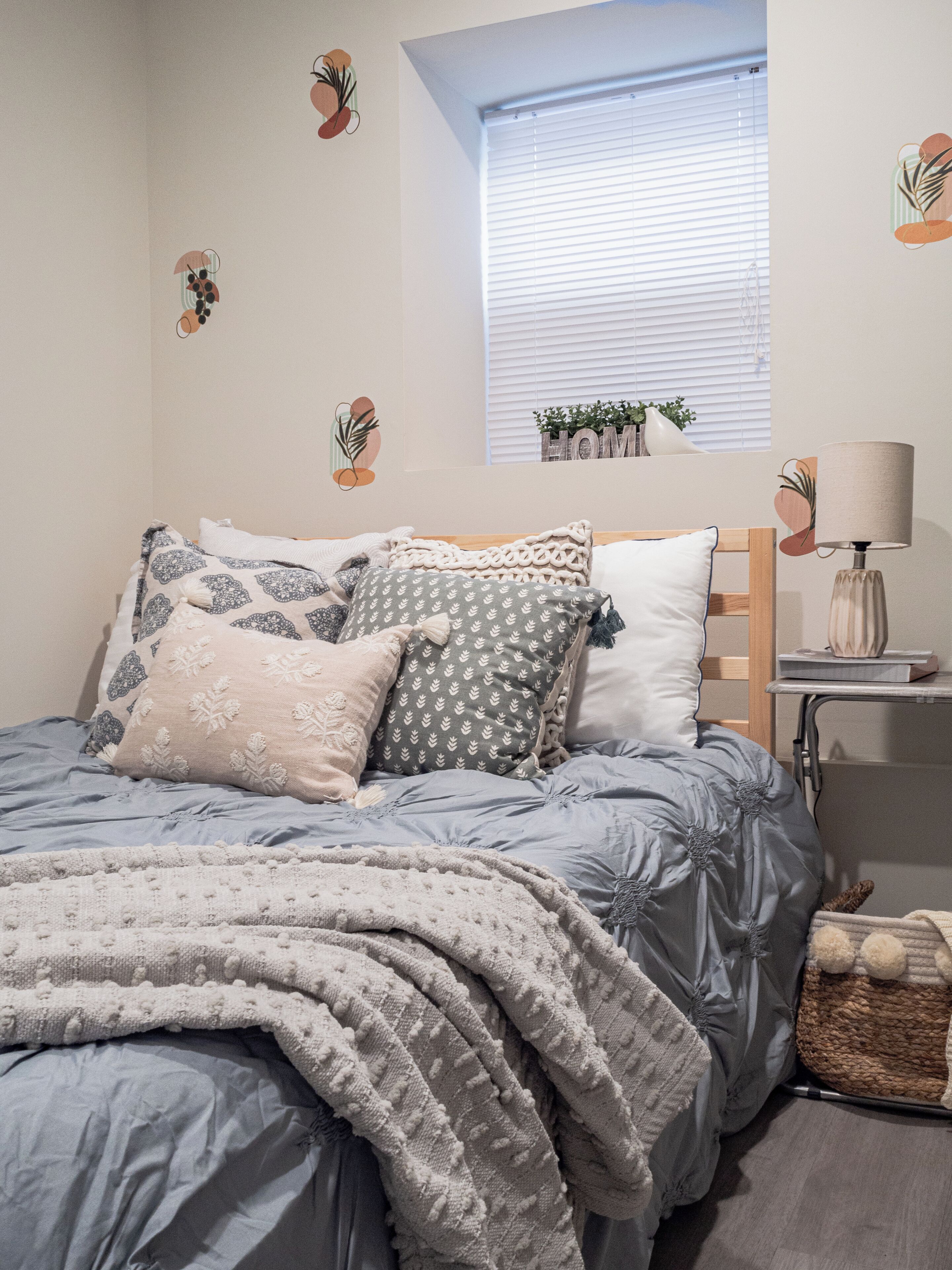 A neatly made bed with patterned bedding, a bedside lamp, and a small window with blinds.