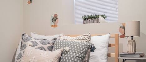 A neatly made bed with patterned bedding, a bedside lamp, and a small window with blinds.