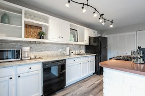 Een moderne keuken met witte kasten, een granieten aanrechtblad, een inbouwvaatwasser, een roestvrijstalen koelkast en een gasfornuis.
