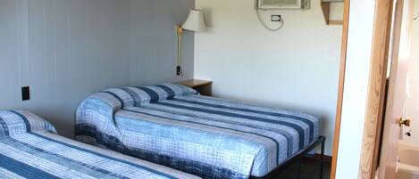 A room with two beds, a nightstand, a lamp, and a wall-mounted air conditioner.
