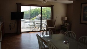A dining area with a table and chairs, a television mounted on the wall, and a view through large sliding doors.