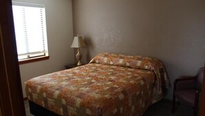 A bedroom with a bed, a chair, a lamp, and a window.