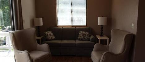 A living room with a sofa, two armchairs, a window with blinds, and two lamps on side tables.