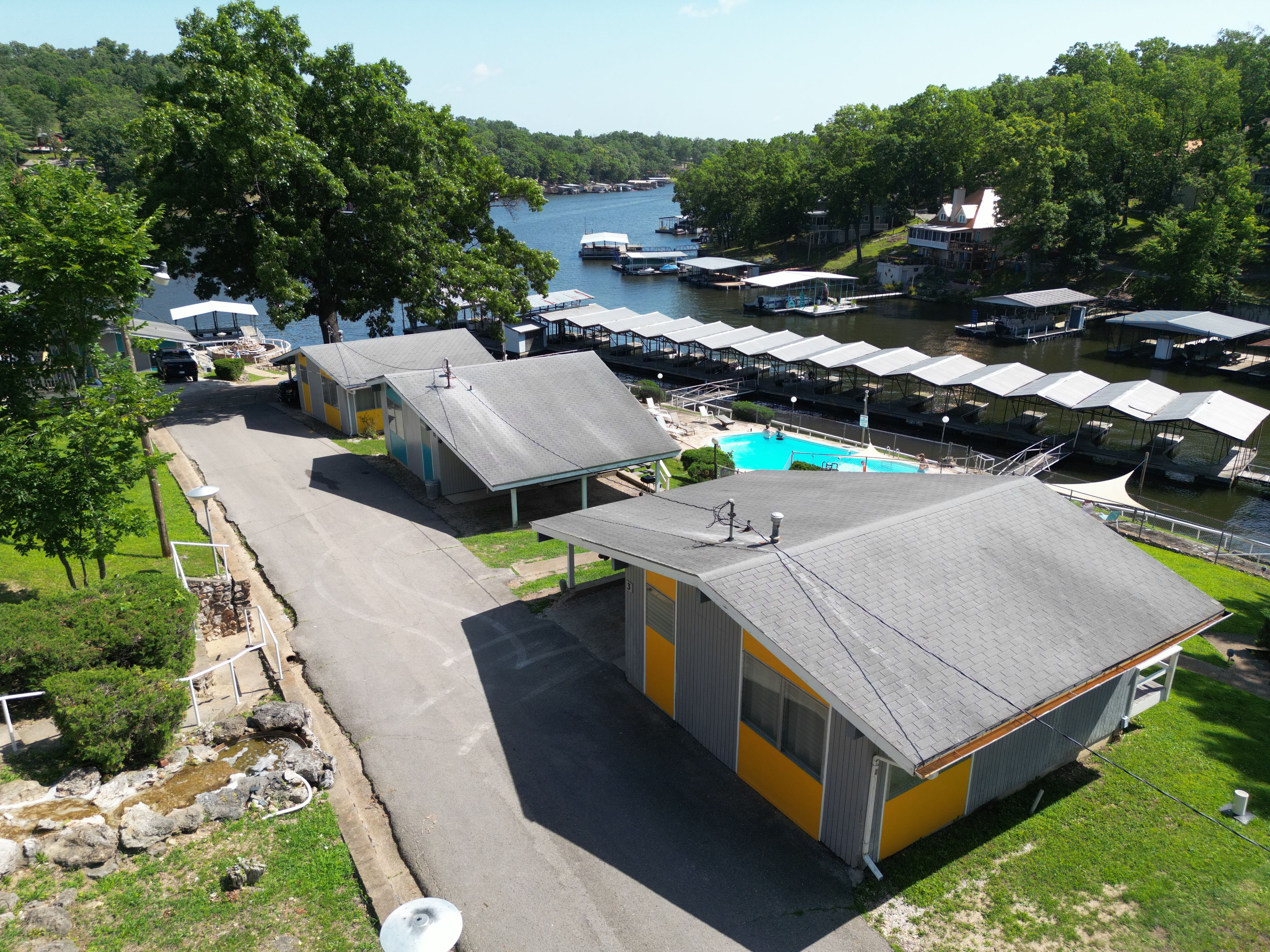 Une propriété au bord du lac comprenant plusieurs petits chalets, une piscine et des bateaux amarrés.