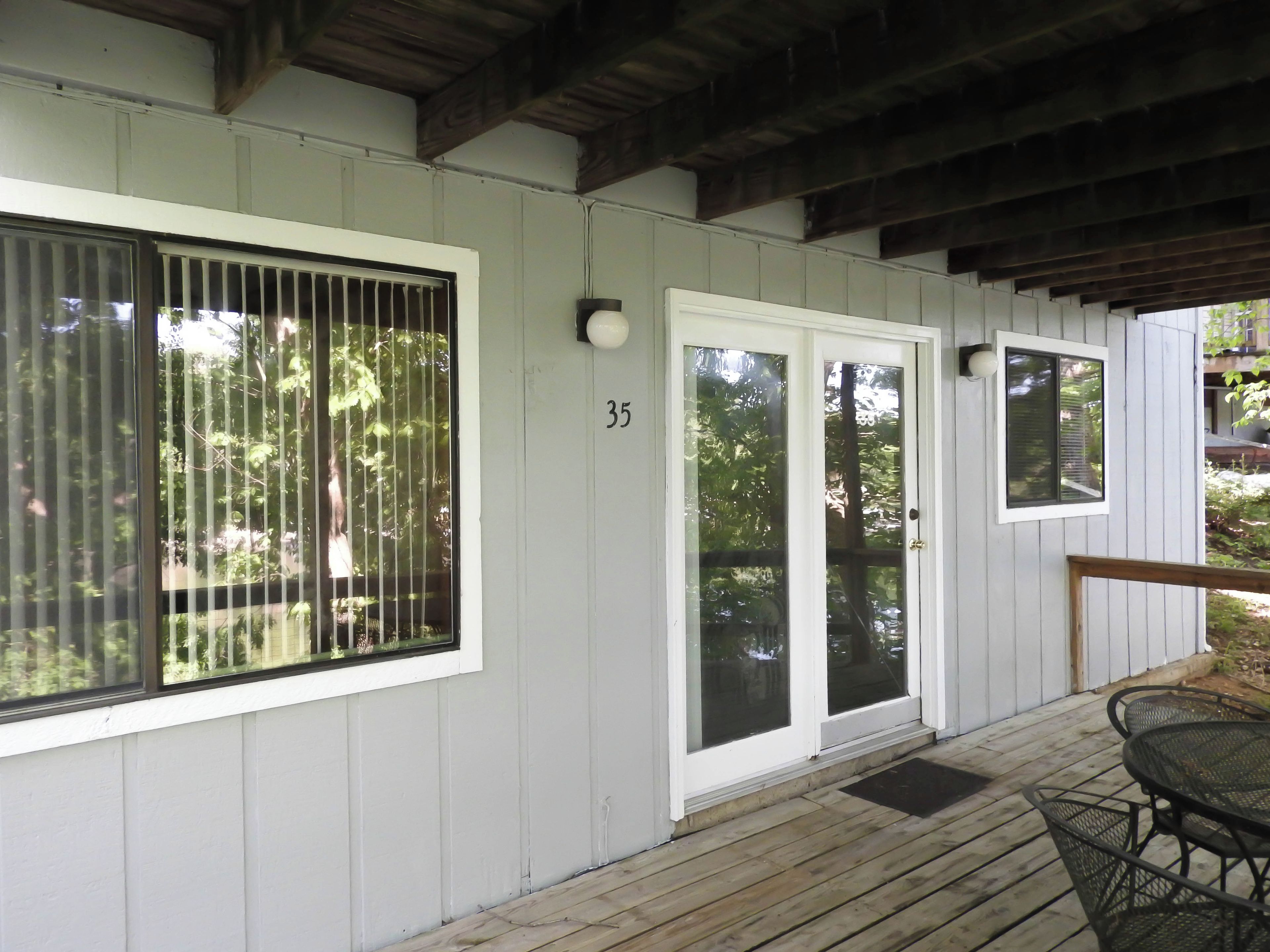 A covered porch with a wooden deck, a number '35' on the wall, and a door with glass panels.