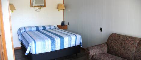 Un dormitorio con cama, mesita de noche, lámpara, sofá y un calentador de pared.