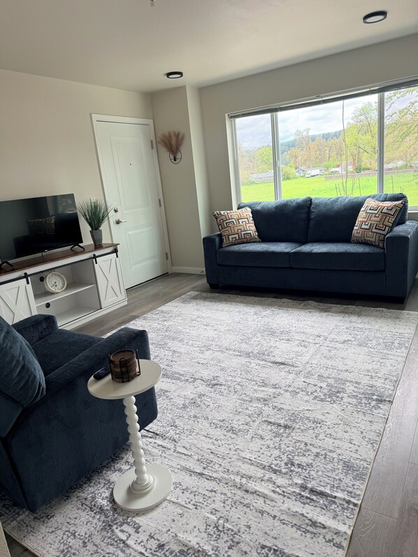 A modern living room with a dark blue sofa, a white coffee table, and a large window with a view of a green landscape.