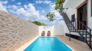 Une piscine avec deux chaises longues, un escalier et un mur blanc orné d’un motif en pierre.