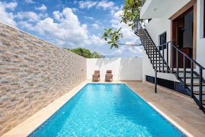 A swimming pool with two lounge chairs, a staircase, and a white wall with a stone pattern.