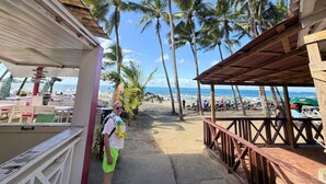 Une vue sur la plage avec une promenade couverte, des palmiers et des parasols de plage.