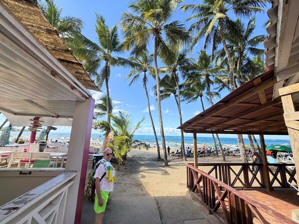 Une vue sur la plage avec une promenade couverte, des palmiers et des parasols de plage.