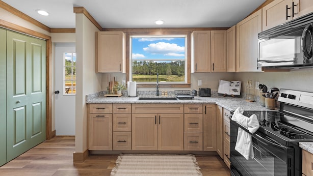 A kitchen with wooden cabinets, a large window with a view, a sink, and a stove. - The Hideaway at Goose Pond Acres- Private Waterfront Retreat (Monticello)