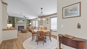 A spacious living room with a fireplace, a dining area with a round table and chairs, and a kitchen in the background. - The Hideaway at Goose Pond Acres- Private Waterfront Retreat (Monticello)