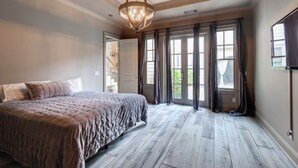 Ein Schlafzimmer mit einem großen Bett, Holzboden, einem Chandelier und Blick durch große Fenster.
