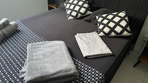 Un lit bien fait, avec une literie à motifs, une table de chevet avec une lampe et une fenêtre avec des rideaux.