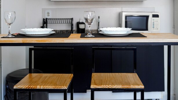 Une cuisine équipée de deux tabourets de bar, d’un four à micro-ondes et d’une étagère sur laquelle est accroché un panneau.