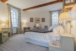 A bedroom with a large bed, two bedside tables, a chair, a dresser, and a window with curtains.