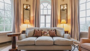 Ein Zimmer mit einem großen Fenster, einem Sofa, einem kleinen runden Tisch und zwei Lampen.