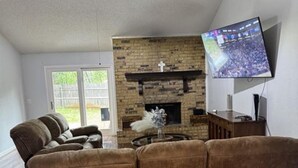 A living room with a brown sofa, a fireplace, a television mounted on the wall, and a ceiling fan. -  3-bedroom house in Arlington, 20 minutes from AT&T Stadium and the Stockyards. (Arlington)