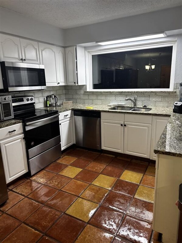 A kitchen with white cabinets, a stainless steel dishwasher, a microwave, an oven, and a sink.