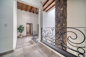 A hallway with a stone column, a potted plant, and a metal railing.