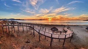 A beach with a wooden boardwalk, a sandy area, and a sunset in the background.