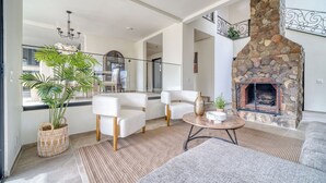 A modern living room with a stone fireplace, white sofas, a round coffee table, and a large potted plant. - Casa Raquel 12 ppl, 5 BD, prime location, steps from Coral y Marina gated com (Ensenada)