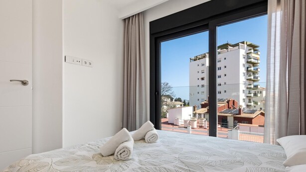 Ein Hotelzimmer mit Bett, Fenster mit Vorhängen und Blick auf Gebäude.
