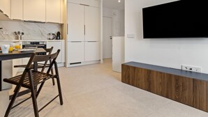 Eine moderne Küche mit weißen Schränken, einer Marmor-Spritzschutzwand, einem Essbereich mit Tisch und Stühlen sowie einem großen Flachbildfernseher an der Wand.