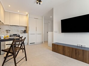A modern kitchen with white cabinets, a marble backsplash, a dining area with a table and chairs, and a large flat-screen TV mounted on the wall. - La Joya 1B. New apartment in Carihuela, 300 m from the beach (Torremolinos)