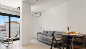 Ein modernes Wohnzimmer mit Sofa, Esstisch und Stühlen, einem Balkon mit Blick sowie einer Klimaanlage.